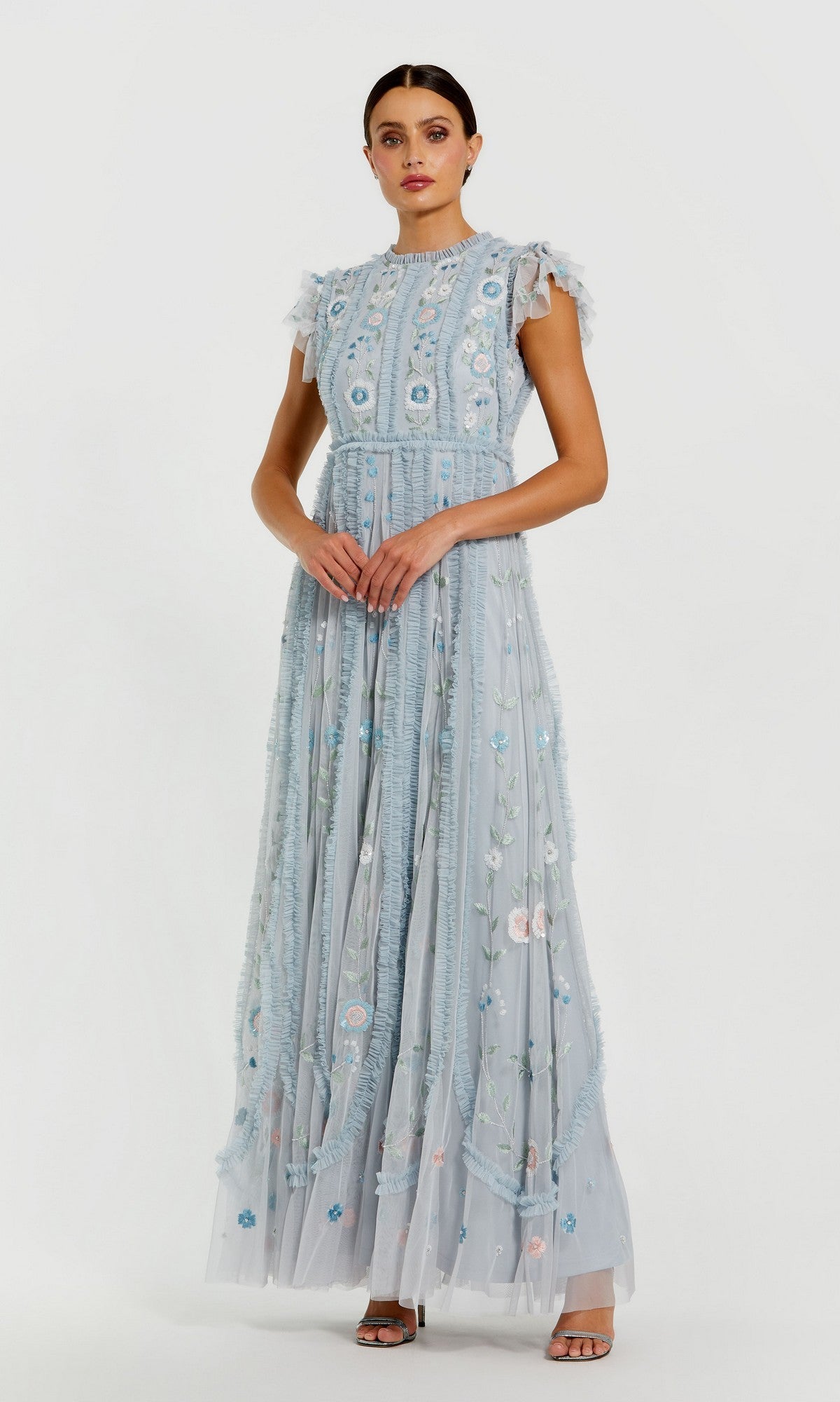 A woman wearing the Mac Duggal 9366 long formal dress in powder blue, featuring floral embroidery and ruffled sleeves, stands against a plain white background.